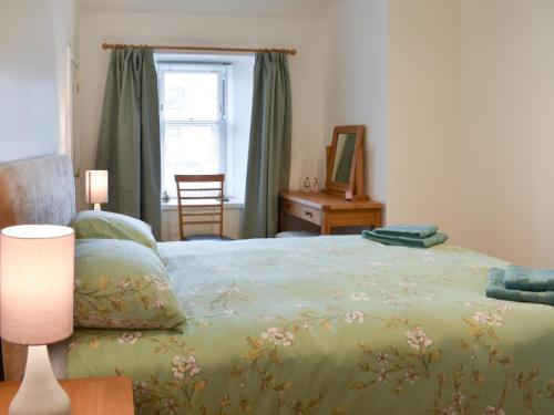 a bedroom with a bed with a green blanket and a window at Rinnes Cottage in Aberlour