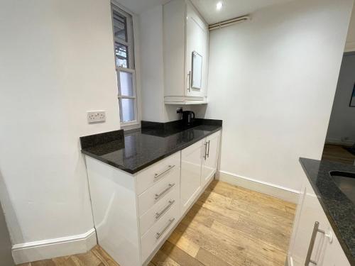 cocina con armarios blancos y encimera negra en Westminster Apartment near River Thames en Londres