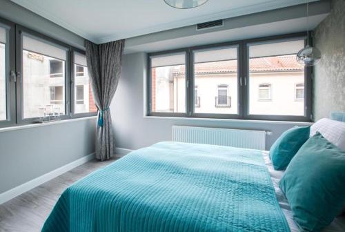 a bedroom with a bed with blue sheets and windows at Apartament Old Town Gdańsk Tartaczna 16D in Gdańsk