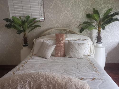 1 dormitorio con 1 cama blanca con almohadas y palmeras en Falklands Guest House, en Johannesburgo