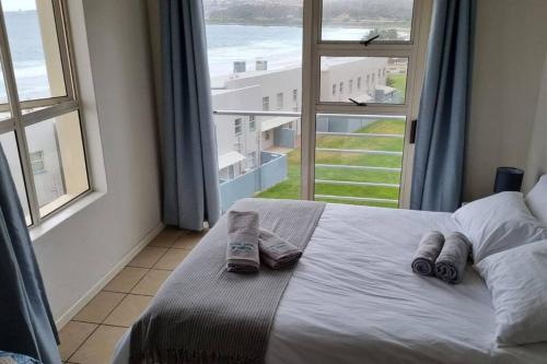 a bed with two slippers on it in a room with windows at La Palma Villas No. 40 in Mossel Bay