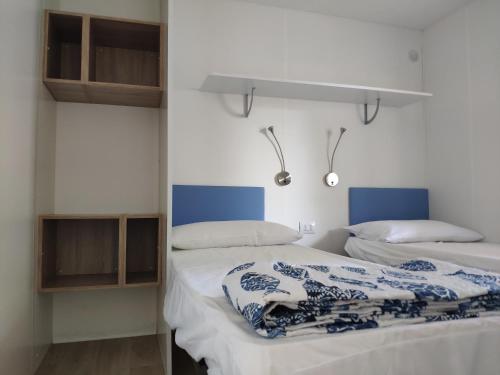 2 camas en una habitación con paredes blancas y detalles azules en Camping Sassabanek, en Iseo