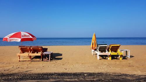 Beach Shalom Luxry Apartment and Villa Colva في كلفا: مجموعة من الكراسي ومظلة على الشاطئ
