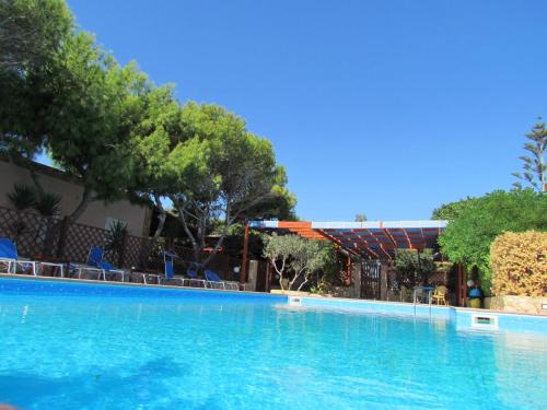 une grande piscine avec des chaises et des arbres bleus dans l'établissement Residence Villalba, à Lampedusa