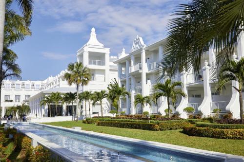 un gran edificio blanco con palmeras y una piscina en Riu Palace Riviera Maya - All Inclusive en Playa del Carmen
