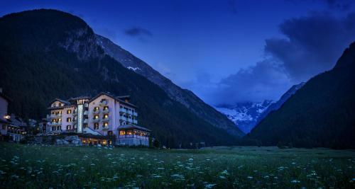 a building in a field with mountains in the background at Bellevue Hotel & SPA in Cogne