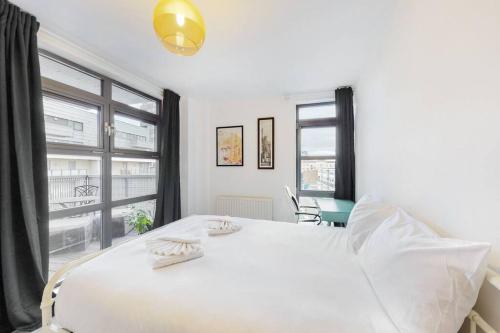 a white bedroom with a large white bed and windows at Modernistic 2-bedroom flat in Shadwell in London