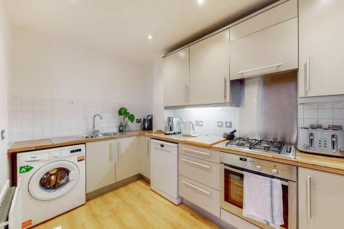 a kitchen with white cabinets and a washing machine at Modernistic 2-bedroom flat in Shadwell in London