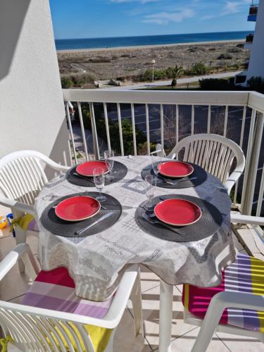 une table avec des assiettes rouges et des verres sur un balcon dans l'établissement Le Sunset plage , vue mer , accès direct plage, 4 personnes, au Barcarès