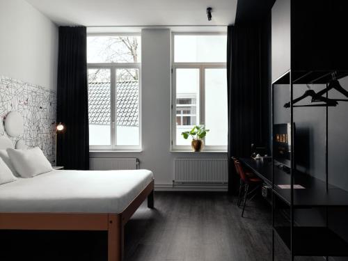 a bedroom with a bed and a desk and two windows at MABI City Centre in Maastricht