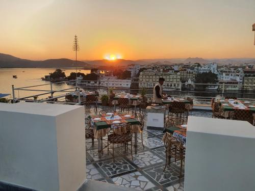 a man sitting at a table on a balcony with the sunset at Hotel Mewar Haveli - At Lake Pichola in Udaipur