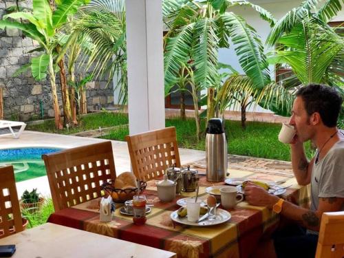 a man sitting at a table drinking a cup of coffee at Residencial Lela d'Fermina in Pombas