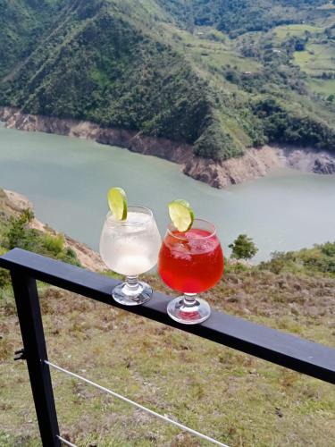 two cocktails sitting on a rail with a view of a mountain at Glamping Mirador del Guavio in Ubalá