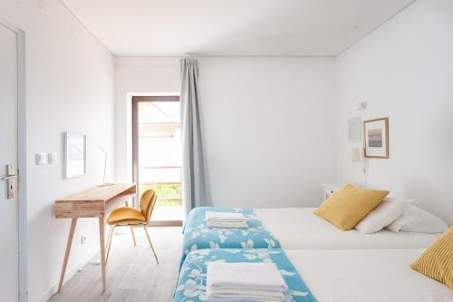 a white bedroom with a bed and a desk at Blue Buddha Beach House in Ericeira