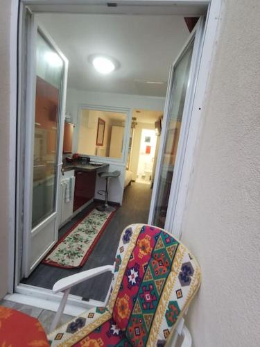 Vistas a una sala de estar con una silla y una cocina en Appartement fonctionnel et équipé en RDC avec petite terrasse couverte au calme en Franqueville-Saint-Pierre