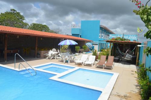 a swimming pool with chairs and a table and an umbrella at Suítes Vovó Zilda in Maragogi