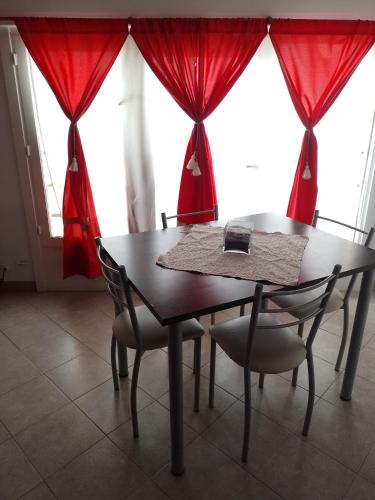 mesa de comedor y sillas con cortinas rojas en Departamento en Comodoro Rivadavia