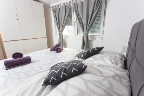 a white bed with purple pillows and a window at Apartman Luka in Vinkovci