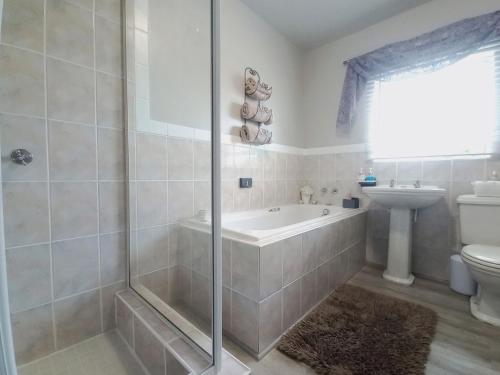 a bathroom with a shower and a tub and a sink at Silverdunes - GardenView in Bettyʼs Bay