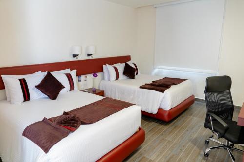 a hotel room with two beds and a chair at Mision Puebla Angelopolis in Puebla