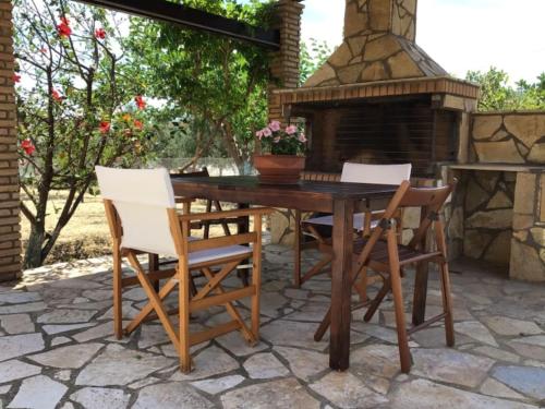 a wooden table and chairs on a patio with a fireplace at An all comforts home in Koroni