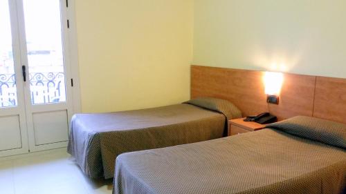 a room with two beds and a door with a window at Hostal Capitol Ramblas in Barcelona