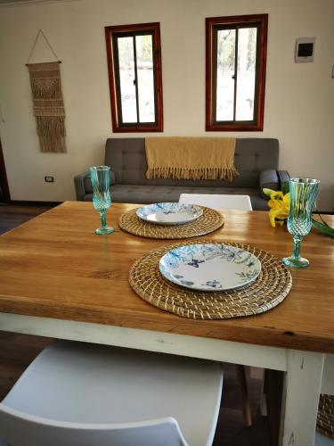 a wooden table with two plates and glasses on it at Cabaña Alma de Montaña, piscina privada in Monte Grande