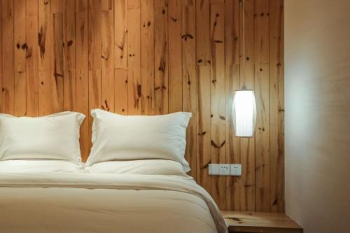 a bed with white pillows and a wooden wall at Villa EN Emerald Valley, Huangshan in Huangshan Scenic Area