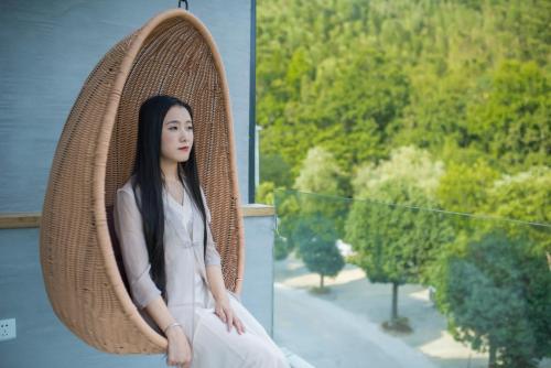 a woman sitting in a wicker chair on a balcony at Villa EN Emerald Valley, Huangshan in Huangshan Scenic Area