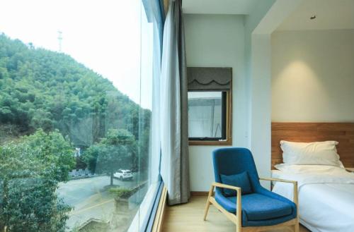 a bedroom with a bed and a blue chair and a window at Villa EN Emerald Valley, Huangshan in Huangshan City