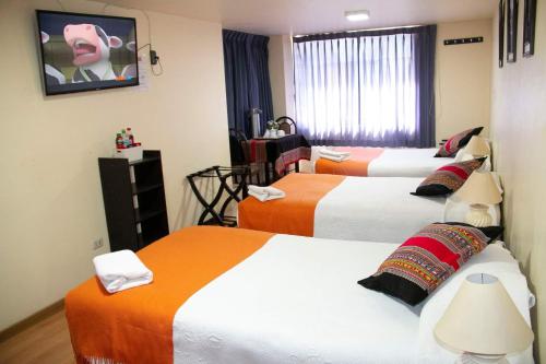 Habitación de hotel con 3 camas con sábanas de color naranja y blanco en Qori Arequipa, en Arequipa