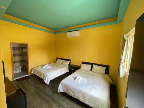 two beds in a room with yellow walls at Kenting Sun Light Inn in Eluan