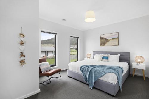 a white bedroom with a bed and a chair at Beach Gum in Apollo Bay