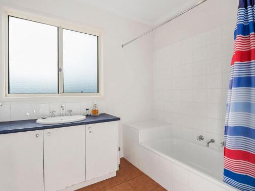 a white bathroom with a tub and a sink and a window at Bimbadeen in Apollo Bay