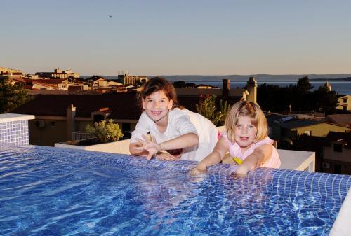 two children are sitting next to a swimming pool at Villa Palloma in Baška Voda