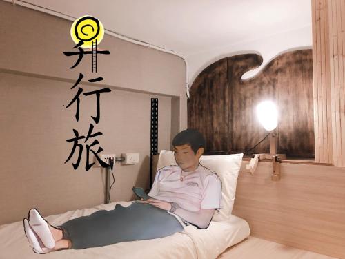 un hombre acostado en una cama con un celular en Hostel of Rising Sun 昇行旅 en Taipéi