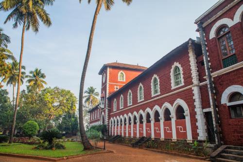a red brick building with palm trees in front of it at Sawantwadi Palace Boutique Art Hotel in Sawantwadi