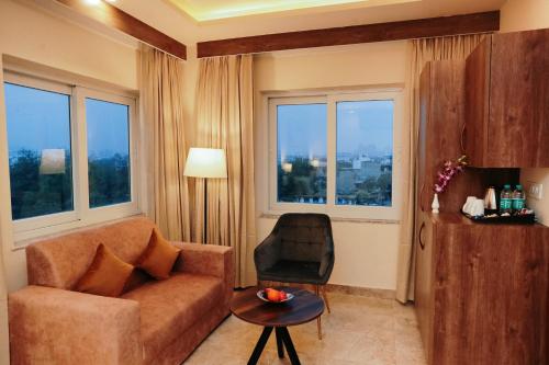 a living room with a couch and a chair and windows at Regenta Inn Greater Noida, 15 Mins to India Expo Mart in Greater Noida