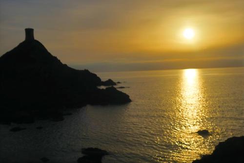 un coucher de soleil sur l'océan avec un phare sur une colline dans l'établissement STUDIO LES CALANQUES, à Ajaccio