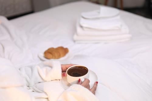 a woman holding a cup of coffee on a bed at The Castle Hotel in Amman