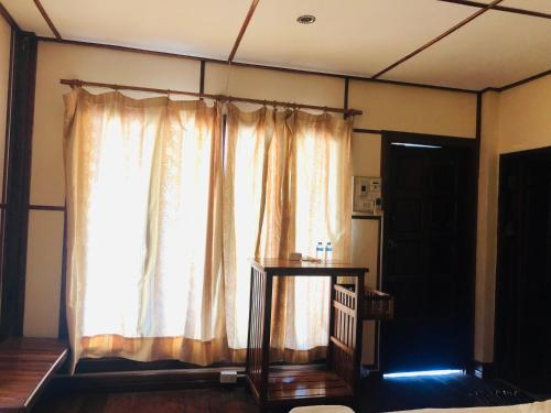 Cette chambre dispose d'une fenêtre avec des rideaux et une table. dans l'établissement Bungalows Le Jardin Organique, à Ban Khouaphan