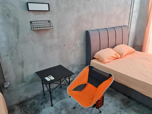 einen orangenen Stuhl neben einem Bett und einem Tisch in der Unterkunft Lot 85 Seremban Town New Cozy Homestay Lobak in Seremban