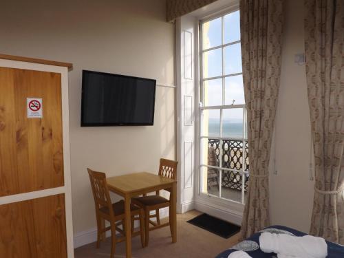 a room with a table and a television and a window at The Edenhurst Guesthouse in Weymouth