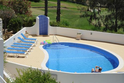 a swimming pool with blue chairs and a woman sitting next to it at Renovated Vale do Milho Golf Apartment with sea view in Carvoeiro