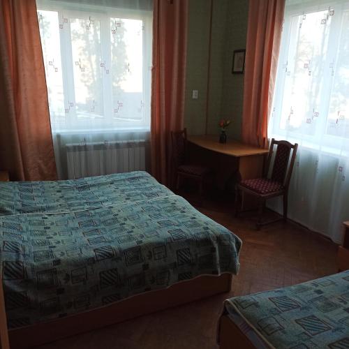 1 dormitorio con 2 camas, mesa y ventanas en Готель-хостел en Truskavets