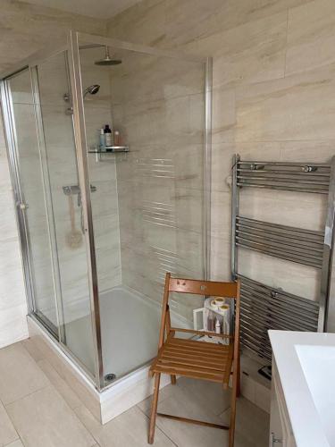 ein Bad mit einer Dusche und einem Holzstuhl in der Unterkunft Cozy home in Croydon