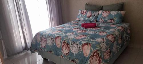 a bed with a blue floral bedspread with a red pillow at 2NIGHTS GUEST HOUSE in Mokopane