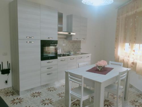 una cucina con armadi bianchi e tavolo e sedie bianchi di Le Camelie appartamento a Bosa
