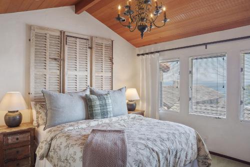a bedroom with a bed and two windows and a chandelier at 3263 Villa by the Sea townhouse in Pacific Grove