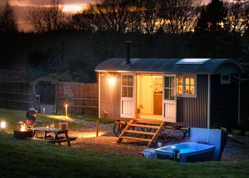 a small shed with a table and a hot tub at Nutkins Luxury Shepherd Hut with hot tub close to Lyme Regis in Uplyme